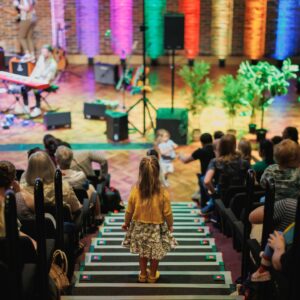 Young girl stood on steps looking down at Turner Sims stage with rainbow lights highlighting the brickwork and audience sat either side