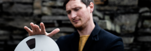 A man holding a film reel and looking at it with a serious expression.