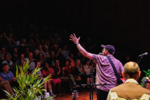 A man waving out to the audience with a mic to his mouth