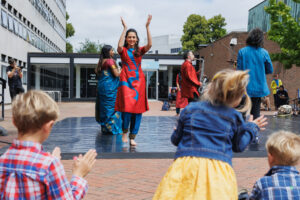 A woman dancing on a stage while children clap along in the foreground