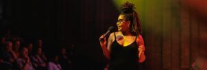 Woman in a black dress and glasses holding a microphone and smiling at the audience at Turner Sims Southampton