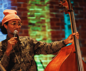 Performer with beanie hat and microphone holding a double bass