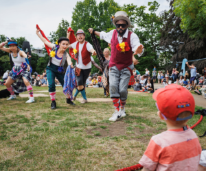 Four performers reaching out to a small child with an audience of families in the background