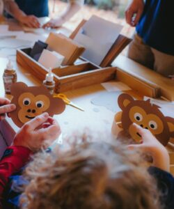 Adult and child working on paper monkey faces on a table full of glue and craft materials