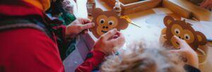 Adult and child working on paper monkey faces on a table full of glue and craft materials