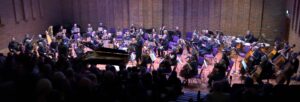 An orchestra seated on the stage under lights