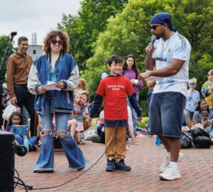 Two young people with a microphone standing with a small child wearing a Turner Sims Team t-shirt standing in front of a crowd