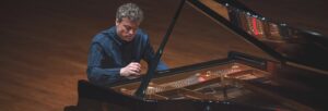 Man wearing a dark coloured shirt playing a grand piano