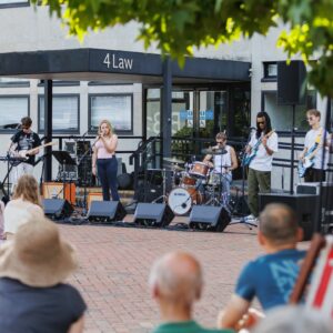 Young people in a band playing outside to a watching audience