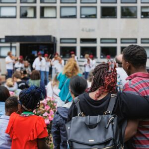 The back of people gathered together outdoors watching musicians on stage.